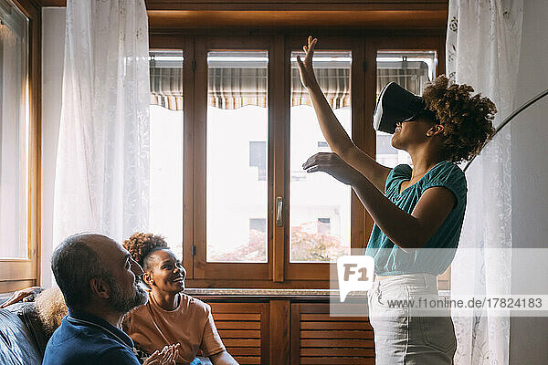 Girl wearing virtual reality simulator gesturing in front of family at home