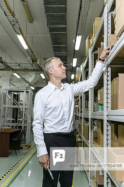 Businessman examining machine part on rack in factory