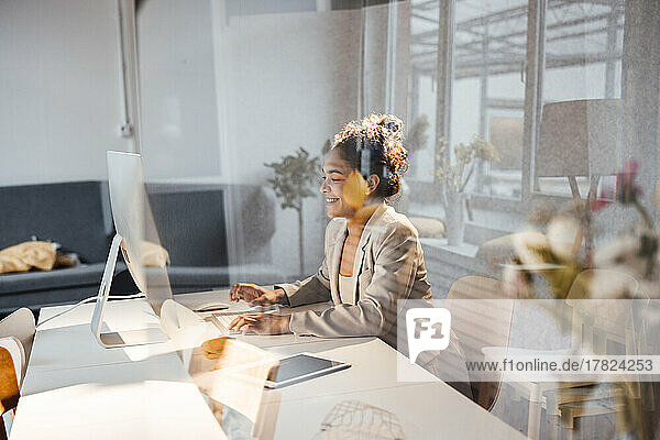 Glückliche junge Geschäftsfrau  die am Schreibtisch im Büro einen Computer benutzt