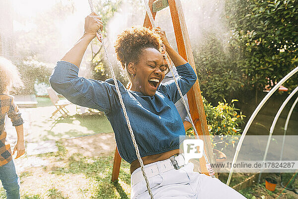 Happy woman with eyes closed swinging in backyard