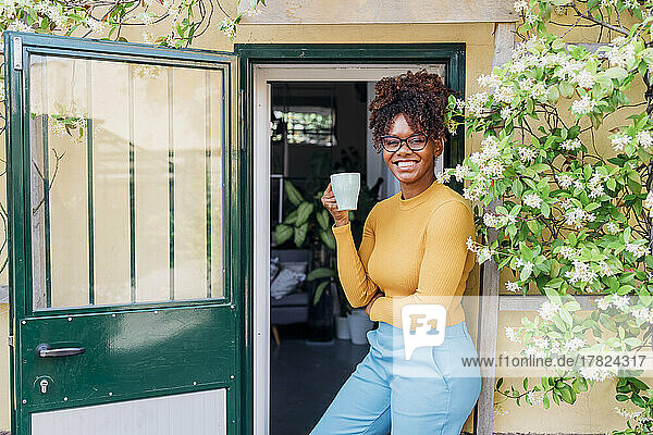 Smiling businesswoman with eyeglasses holding coffee cup at doorway