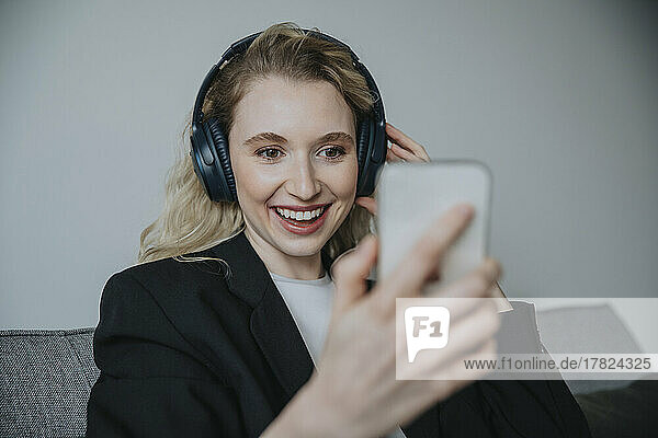 Smiling businesswoman wearing headphones and looking at smart phone