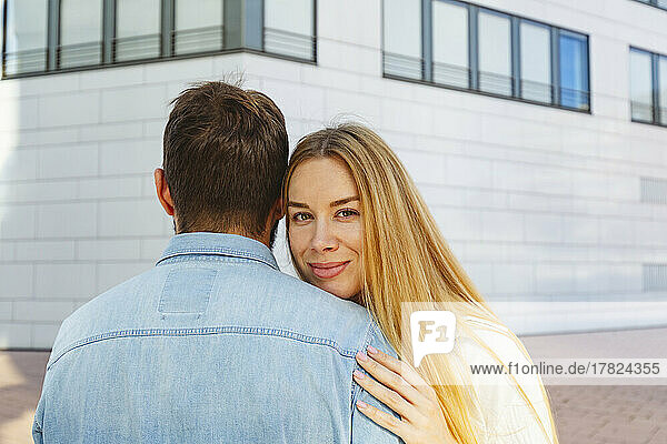 Smiling blond woman hugging man in front of building