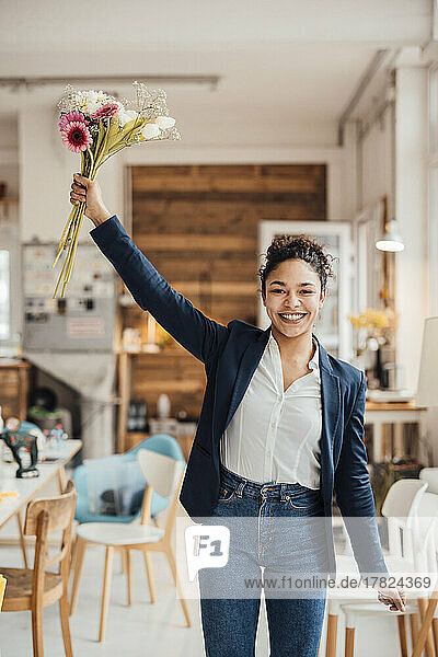 Cheerful young businesswoman standing with flowers in office