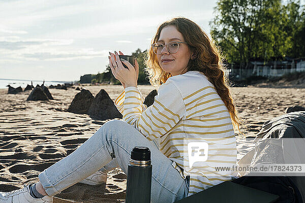 Young woman holding cup sitting at beach