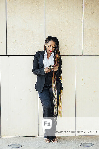 Young businesswoman using mobile phone in front of wall