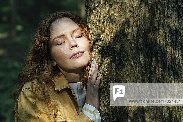 Woman with eyes closed embracing tree in forest