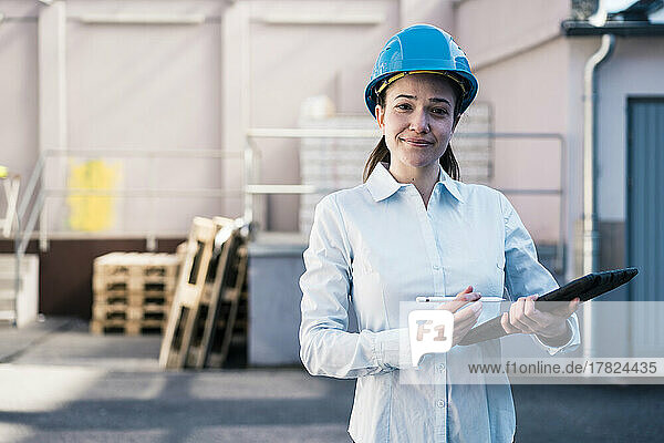 Lächelnde Architektin im Arbeitshelm mit Tablet-PC in der Fabrik