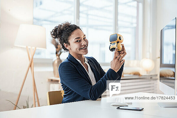 Happy businesswoman with AI toy robot sitting at desk in office