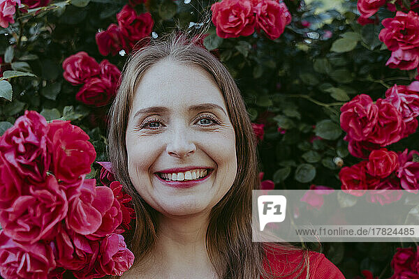 Happy woman amidst bush of red roses