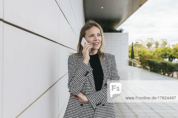 Businesswoman talking on phone standing by wall