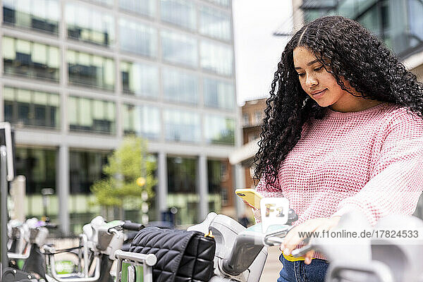Young woman unlocking electric push scooter through smart phone
