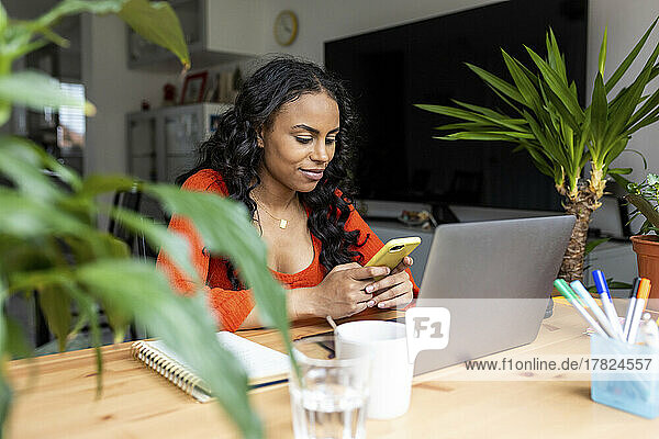 Smiling freelancer using smart phone at desk in home office