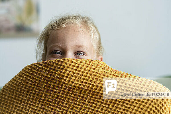 Girl hiding face under blanket at home