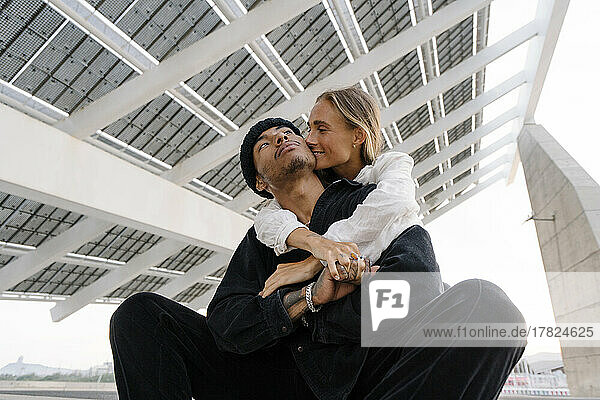 Lächelnde junge Frau umarmt ihren Freund  der unter einem Dach sitzt