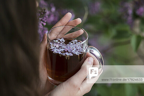 Hände einer Frau  die eine Teetasse mit lila Blüten hält