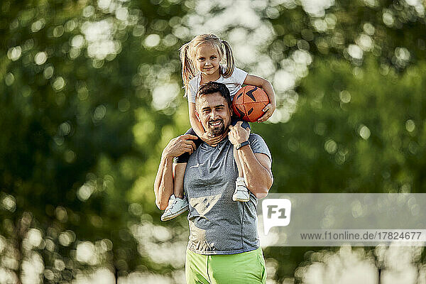 Smiling girl with rugby ball sitting on father's shoulders
