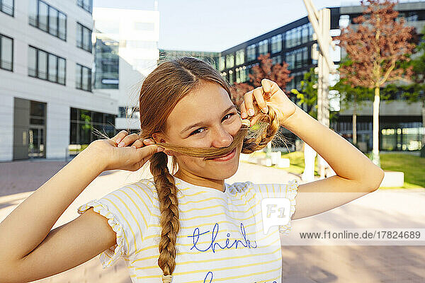 Smiling girl making mustache with hair standing in front of building