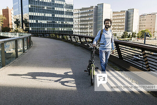 Smiling man with bicycle walking on footbridge