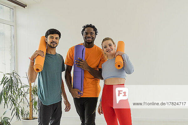 Smiling woman and men holding exercise mats in yoga studio