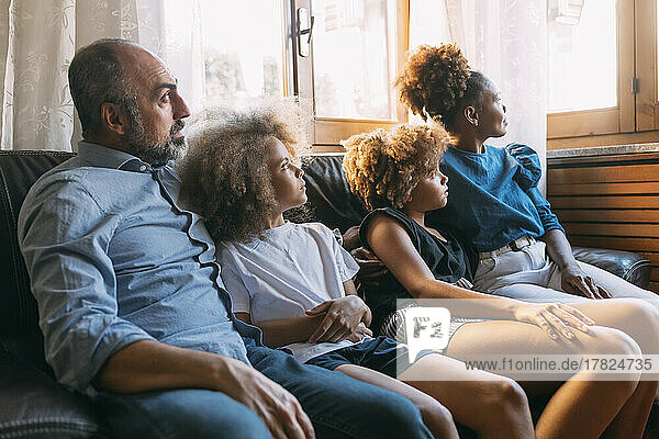 Mann mit Familie schaut durchs Fenster und sitzt zu Hause auf dem Sofa