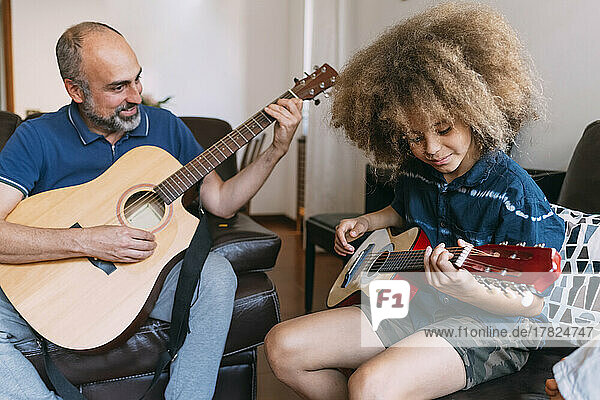 Smiling man teaching son to play guitar at home