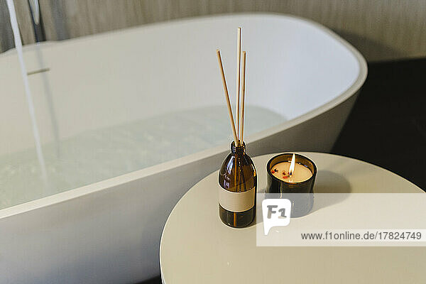 Incense sticks by burning scented candle on table near bathtub