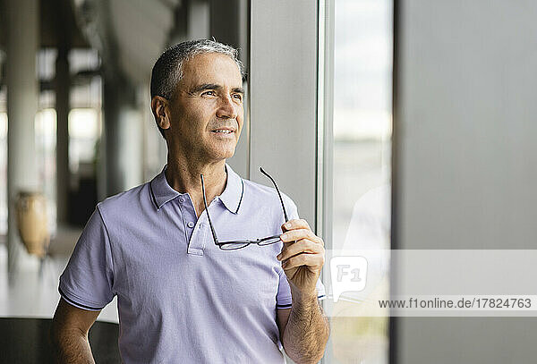 Businessman holding eyeglasses looking out of window at office