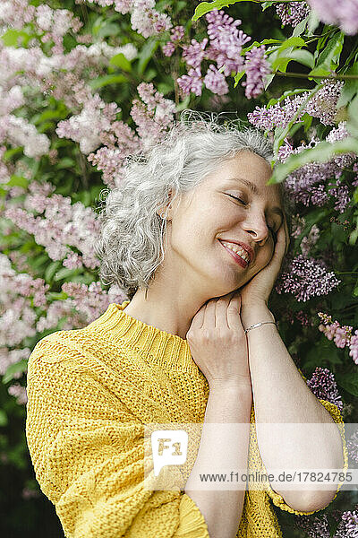 Smiling woman with eyes closed standing by lilac tree