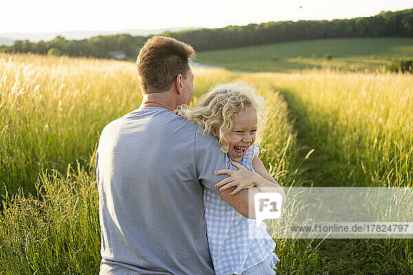Fröhliche Tochter genießt es mit ihrem Vater an einem sonnigen Tag auf dem Feld