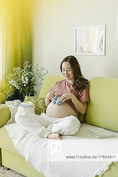 Happy woman with baby booties sitting on sofa at home