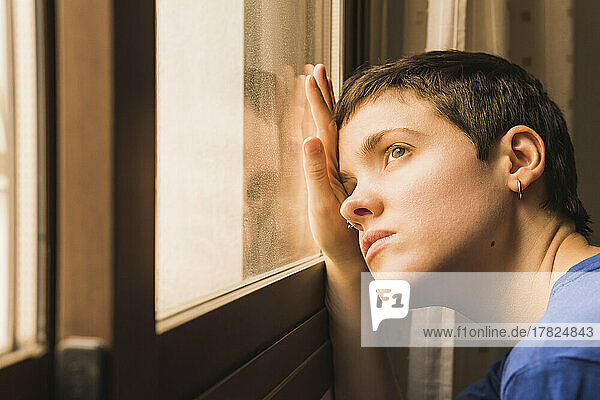 Depressed woman looking through window at home