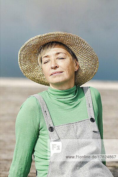 Mature woman wearing hat sitting with eyes closed on sunny day