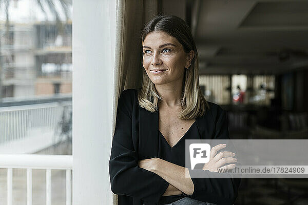 Smiling businesswoman with arms crossed looking through window at hotel