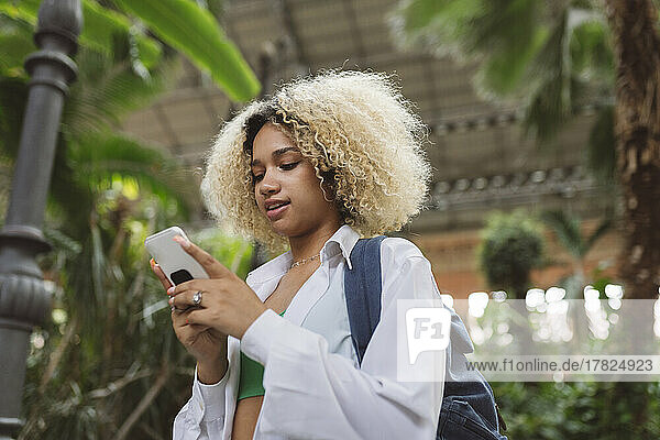Woman with curly hair using smart phone in front of trees