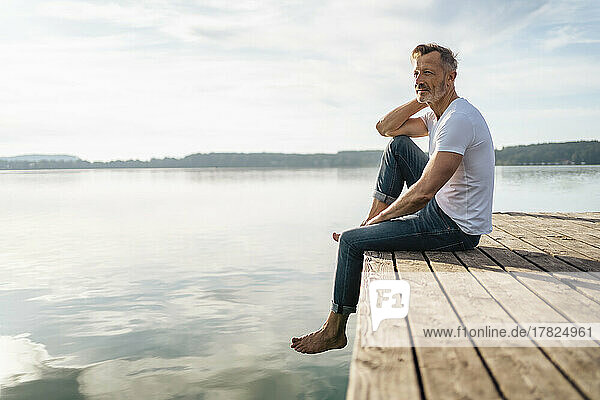 Thoughtful mature man sitting at the edge of pier by lake