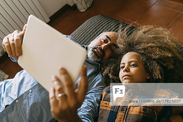 Father sharing tablet PC with son lying on bed at home