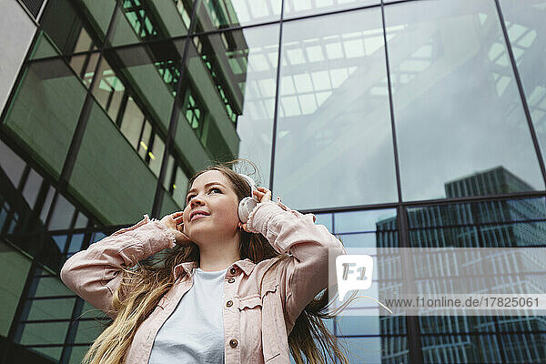 Smiling woman wearing wireless headphones standing in front of building