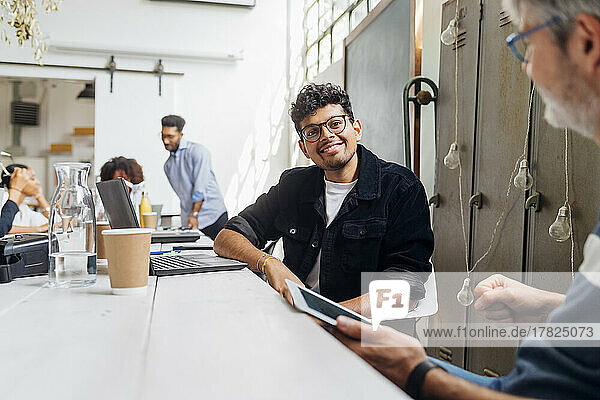 Smiling businessman with eyeglasses by colleagues in office