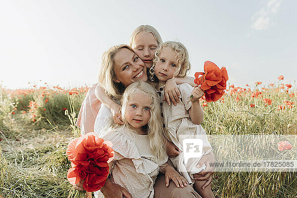 Smiling woman with daughters holding flower in meadow