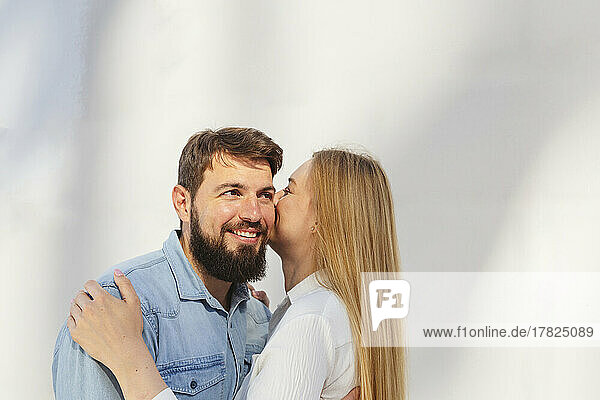 Blond woman kissing man on cheek standing in front of wall