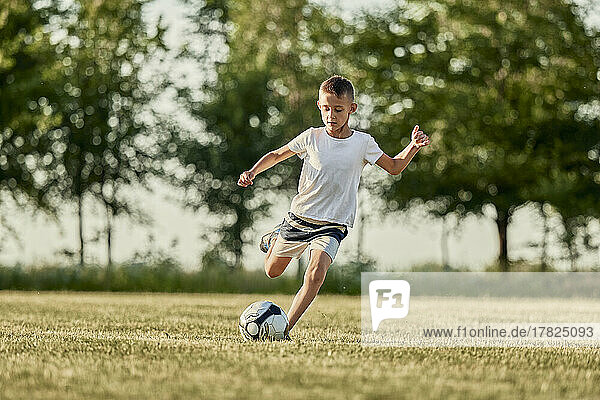 Boy kicking soccer ball at sports field on sunny day