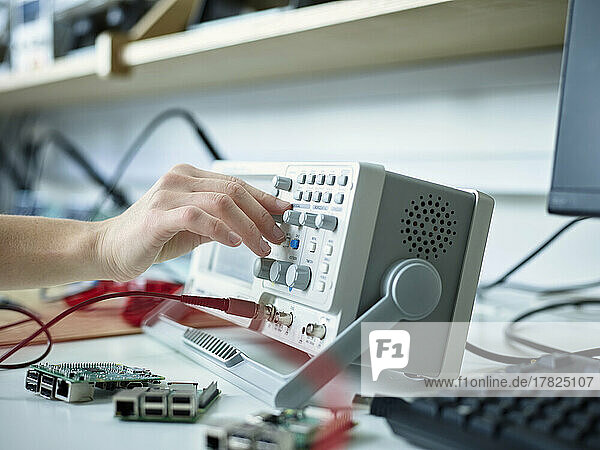 Hand of technician adjusting oscilloscope in electronic laboratory