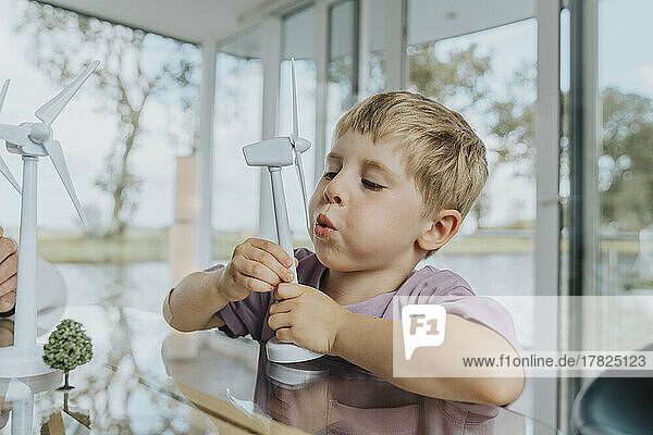 Boy blowing on wind turbine model at home