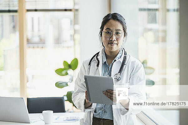 Smiling female doctor with tablet PC standing in office