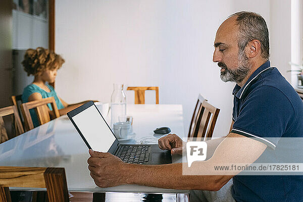 Mann benutzt Laptop und sitzt mit Tochter am Tisch