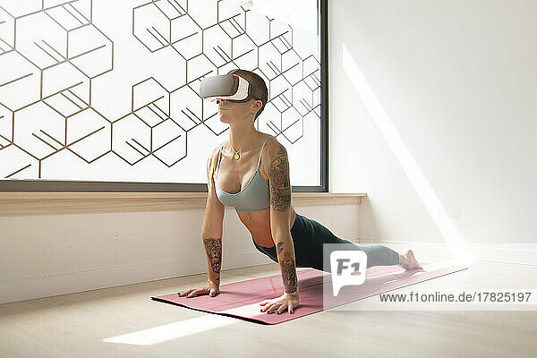 Woman wearing virtual reality headset doing yoga on exercise mat in studio