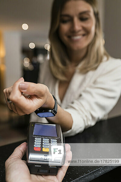 Lächelnde Frau  die im Restaurant mit einer Smartwatch bezahlt