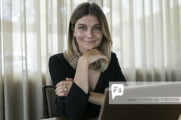 Smiling businesswoman sitting with hand on chin at desk