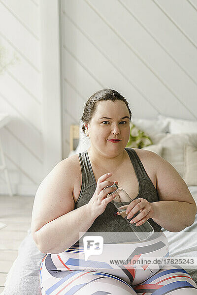 Woman holding water bottle sitting on bed at home